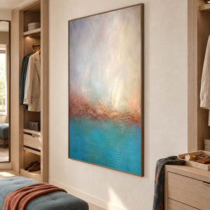 Turquoise coastal painting with a warm shoreline and a luminous pale sky in a brown wood frame in a dressing area.