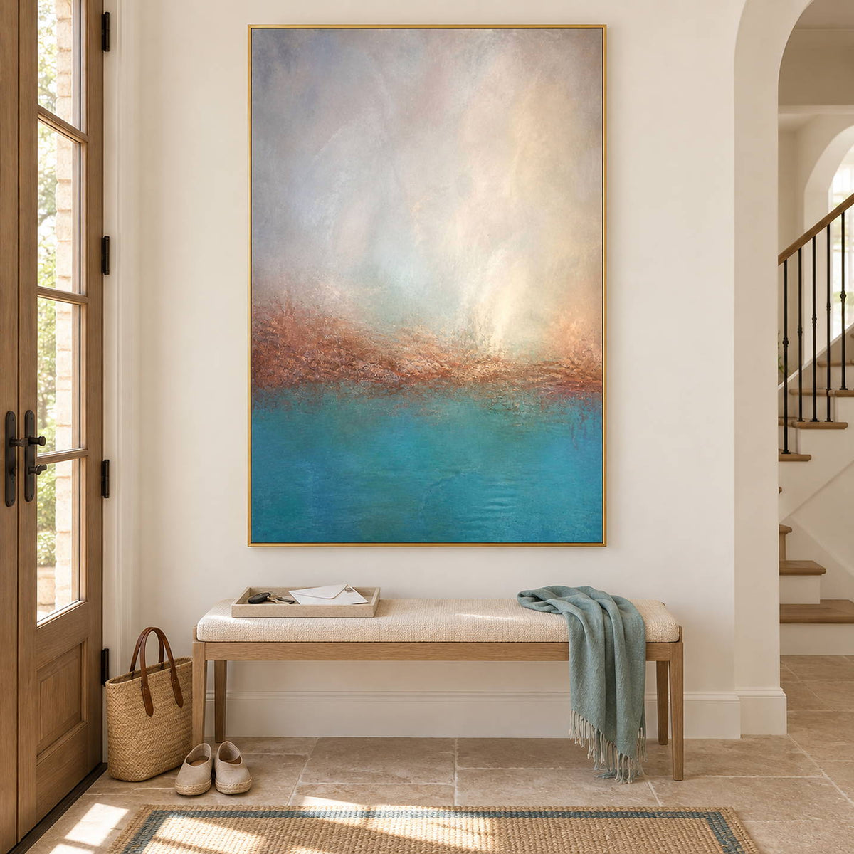 Turquoise coastal painting with a warm shoreline and a luminous pale sky in a gold frame in an entryway.