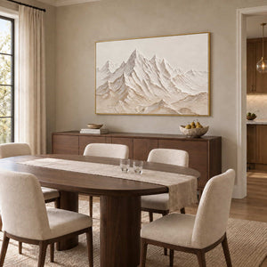 Mountains Keeping Watch in a gold frame above a wood sideboard behind a dining table with cream chairs.