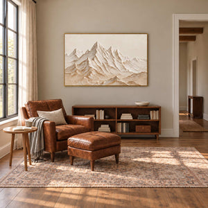 Mountains Keeping Watch in a gold frame above a low bookcase behind a brown leather armchair and footstool.
