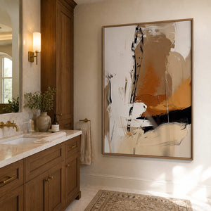 Wood framed warm abstract artwork beside a stone vanity and brass bathroom fixtures.