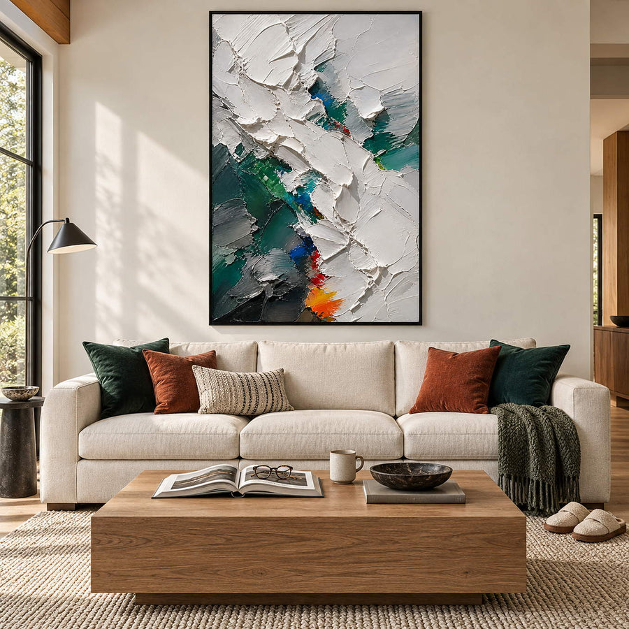 Abstract painting with thick white, emerald, charcoal, and blue palette-knife layers in a black frame in a living room.