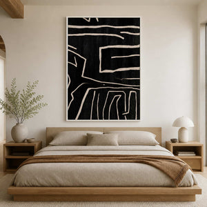 White framed abstract line painting hangs above a beige bed and brown throw.