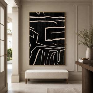 Gold framed abstract line painting above a cream bench in a paneled entryway.