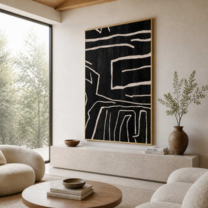 Black abstract line painting in a gold frame beside curved cream seating.
