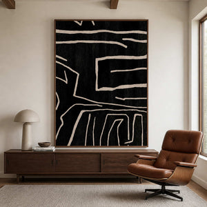 Wood framed black abstract painting beside a brown leather reading chair.