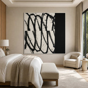 White framed black and white abstract artwork beside a bed and cream bedroom reading chair.