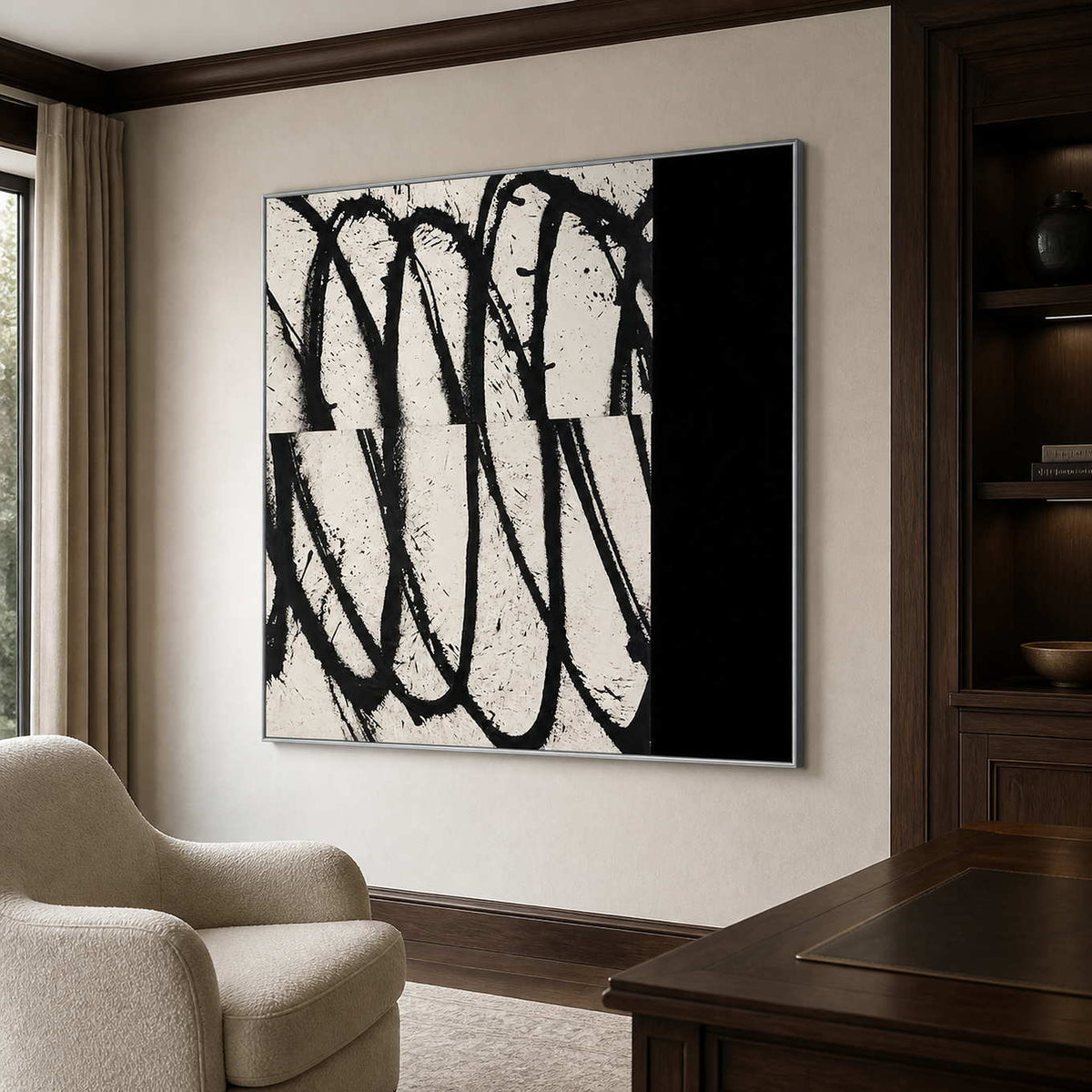 Silver framed looping abstract artwork beside bookshelves and a wooden desk in a home office.