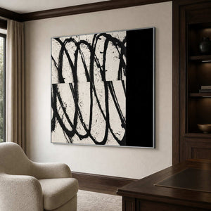 Silver framed looping abstract artwork beside bookshelves and a wooden desk in a home office.