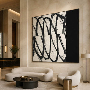 Black framed square abstract artwork above cream seating beside a round black hotel lobby table.