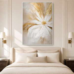 White-framed floral artwork above a cream bed, with long raised petals and golden accents against a warm pale wall.