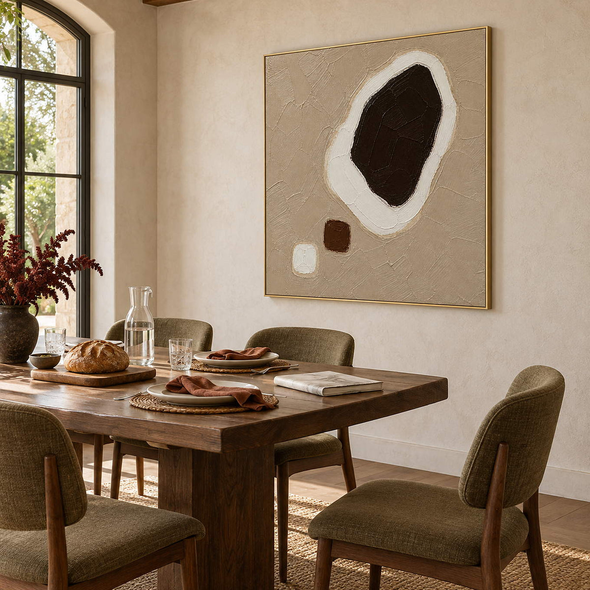 Taupe abstract painting with a large dark brown shape edged in white and two small forms in a gold frame in a dining room.