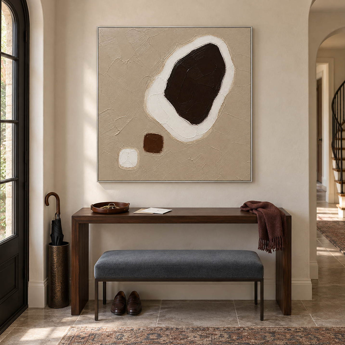Taupe abstract painting with a large dark brown shape edged in white and two small forms in a silver frame in an entryway.