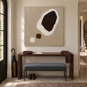 Taupe abstract painting with a large dark brown shape edged in white and two small forms in a silver frame in an entryway.