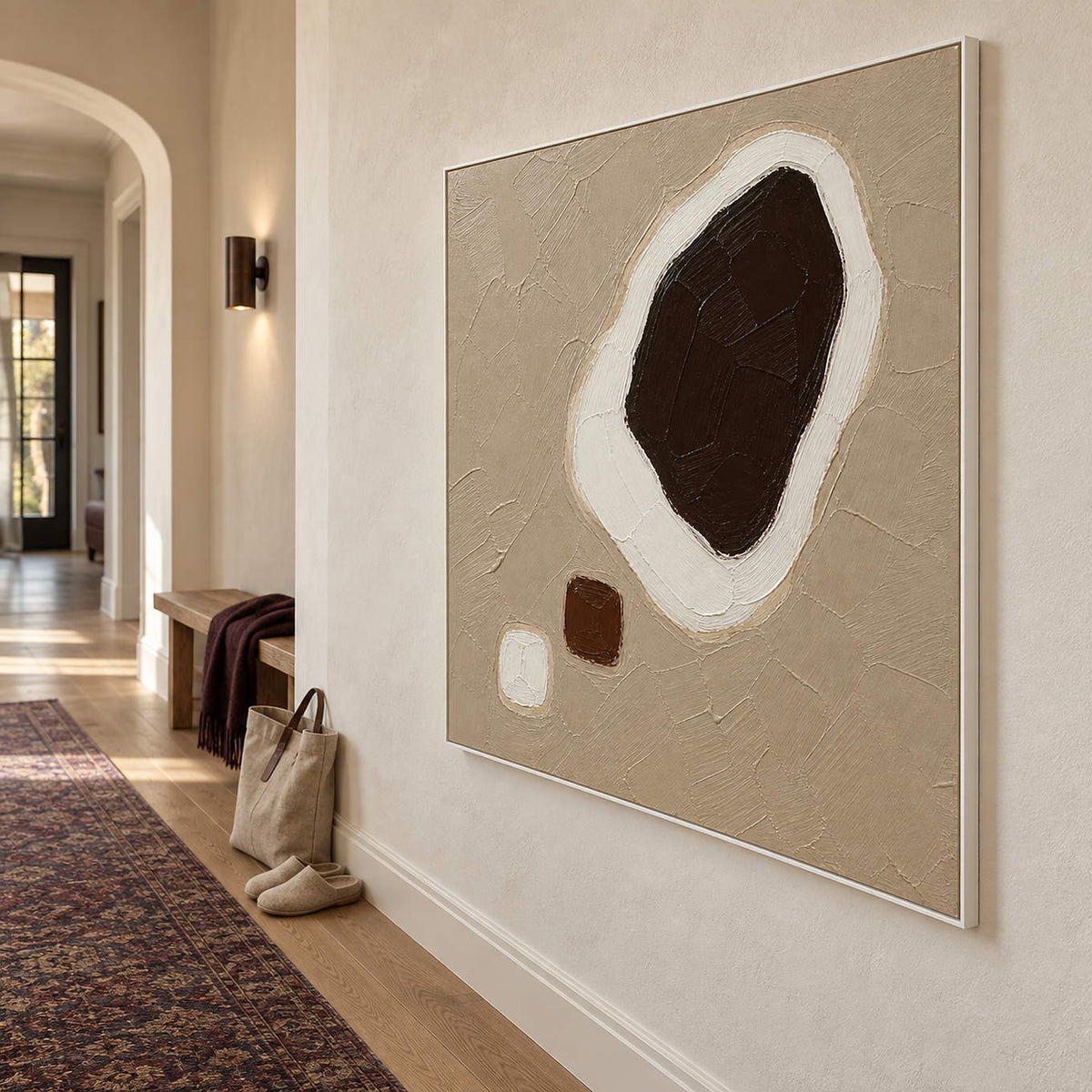 Taupe abstract painting with a large dark brown shape edged in white and two small forms in a white frame in a hallway.