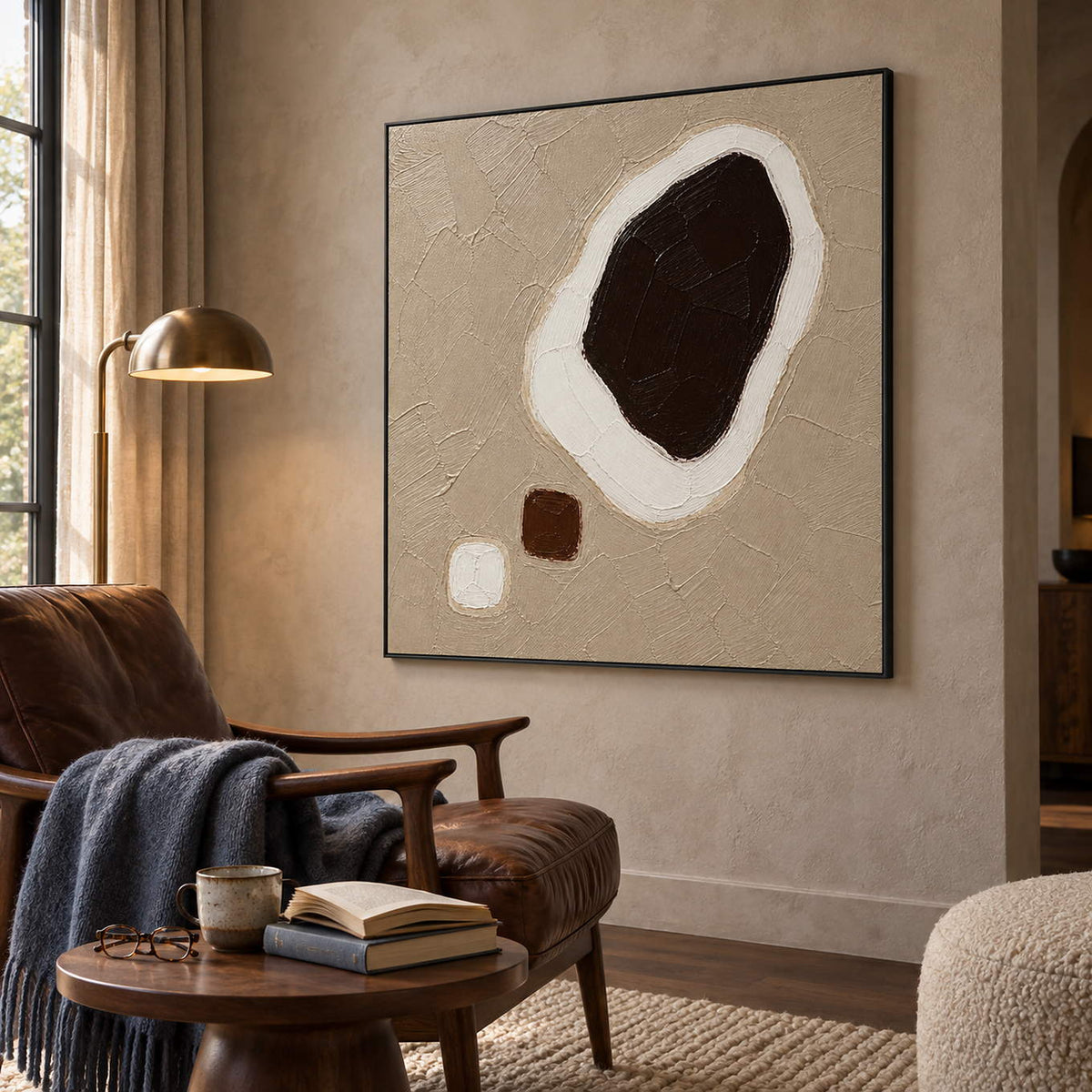 Taupe abstract painting with a large dark brown shape edged in white and two small forms in a black frame in a reading room.