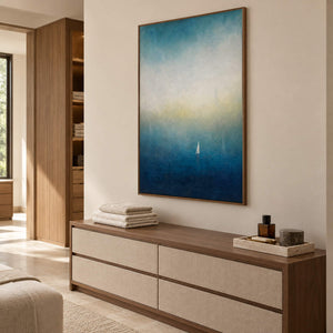 Atmospheric coastal painting with a white sail drifting across deep teal water, displayed in a bathroom dry area in a brown wood frame.