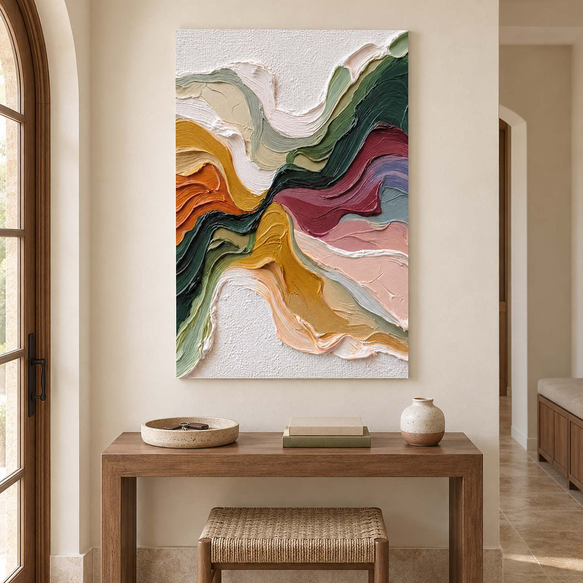 Tall abstract artwork above a wood console and woven stool beside an arched window.