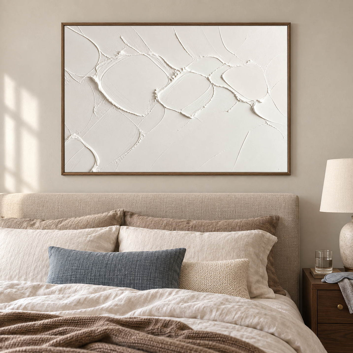 Chalk-white abstract relief painting with raised irregular seams in a brown wood frame in a bedroom.