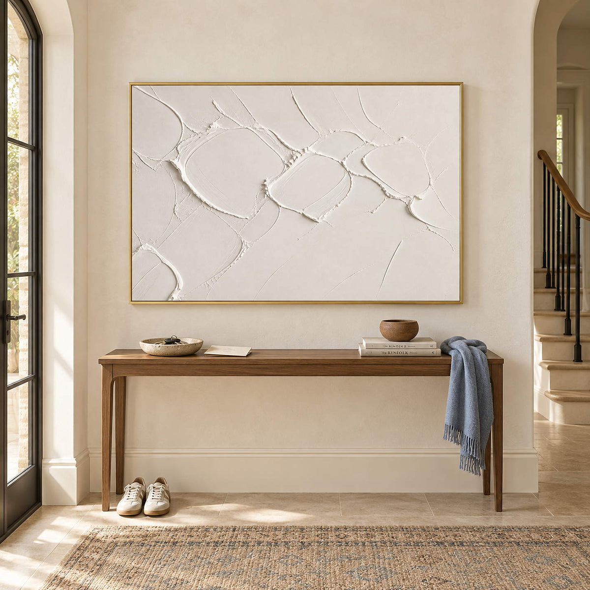 Chalk-white abstract relief painting with raised irregular seams in a gold frame in an entryway.