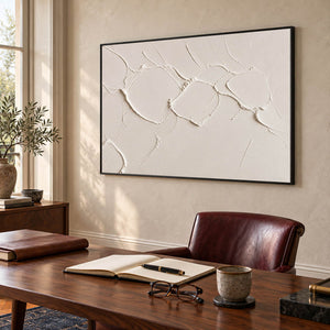Chalk-white abstract relief painting with raised irregular seams in a black frame in a home office.