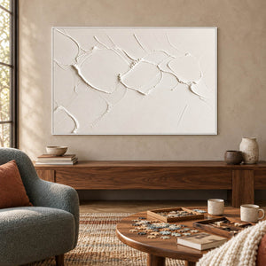 Chalk-white abstract relief painting with raised irregular seams in a white frame in a lounge.