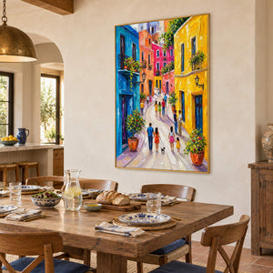 Colorful street painting with people, bright facades, and flowered balconies in a gold frame in a dining room.