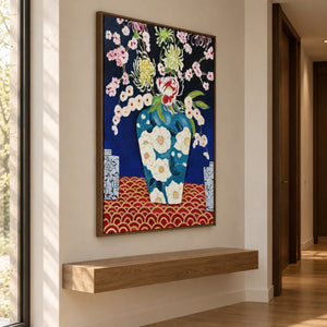 Flowers in a blue floral-patterned vase above a red surface with repeated gold-colored arcs in an artwork with a brown wood-look frame, displayed above a floating wooden bench in a hallway.