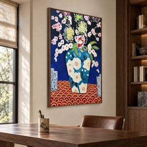 Flowers in a blue floral-patterned vase above a red surface with repeated gold-colored arcs in an artwork with a brown wood-look frame, displayed in a study with a desk.