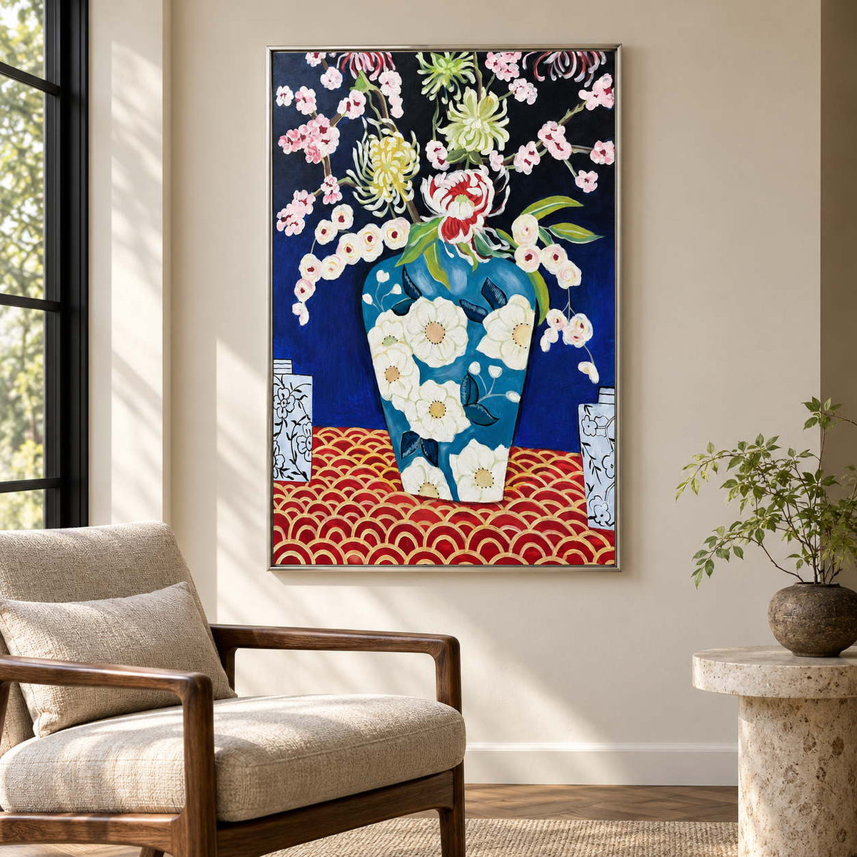 Artwork showing flowers in a blue floral-patterned vase above a red surface with repeated gold-colored arcs beside a reading chair, with a silver-colored frame.