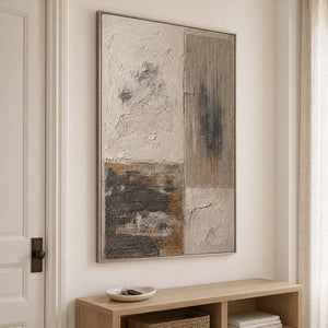 Weathered ivory and beige textures with gray blocks and dark marks in a silver frame, displayed above an entryway console.