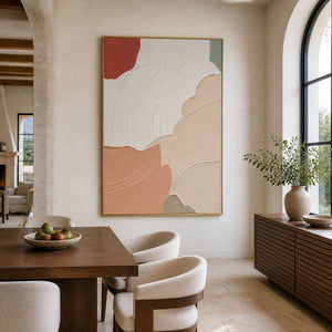 Gold-framed textured peach artwork beside a wooden dining table, cream chairs, and arched window.