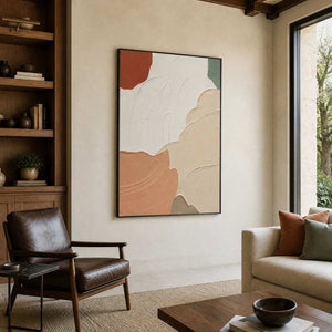 Black-framed peach and white artwork beside wooden bookshelves and a leather reading chair.