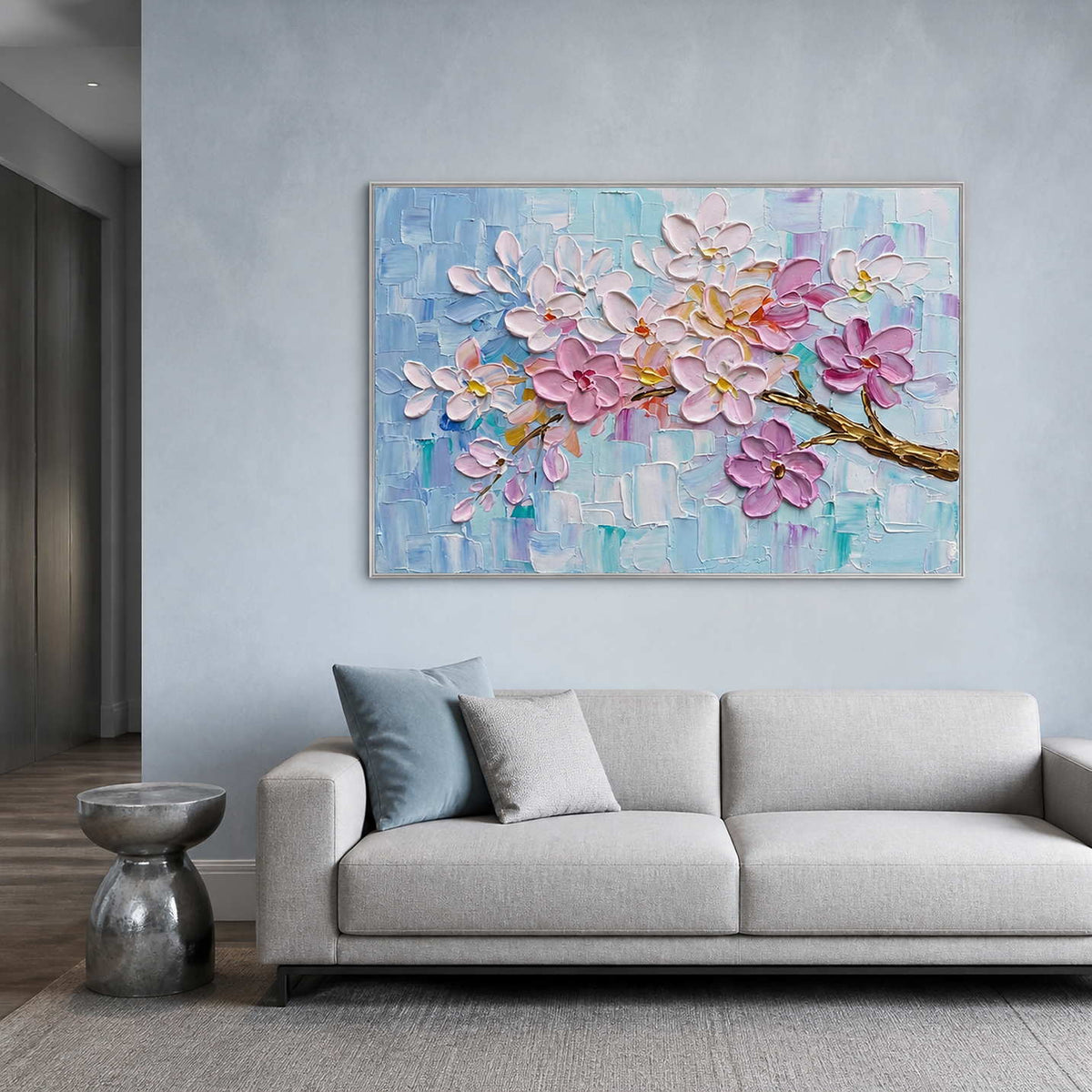 Blush blossom artwork displayed above a cool blue-gray living room sofa.