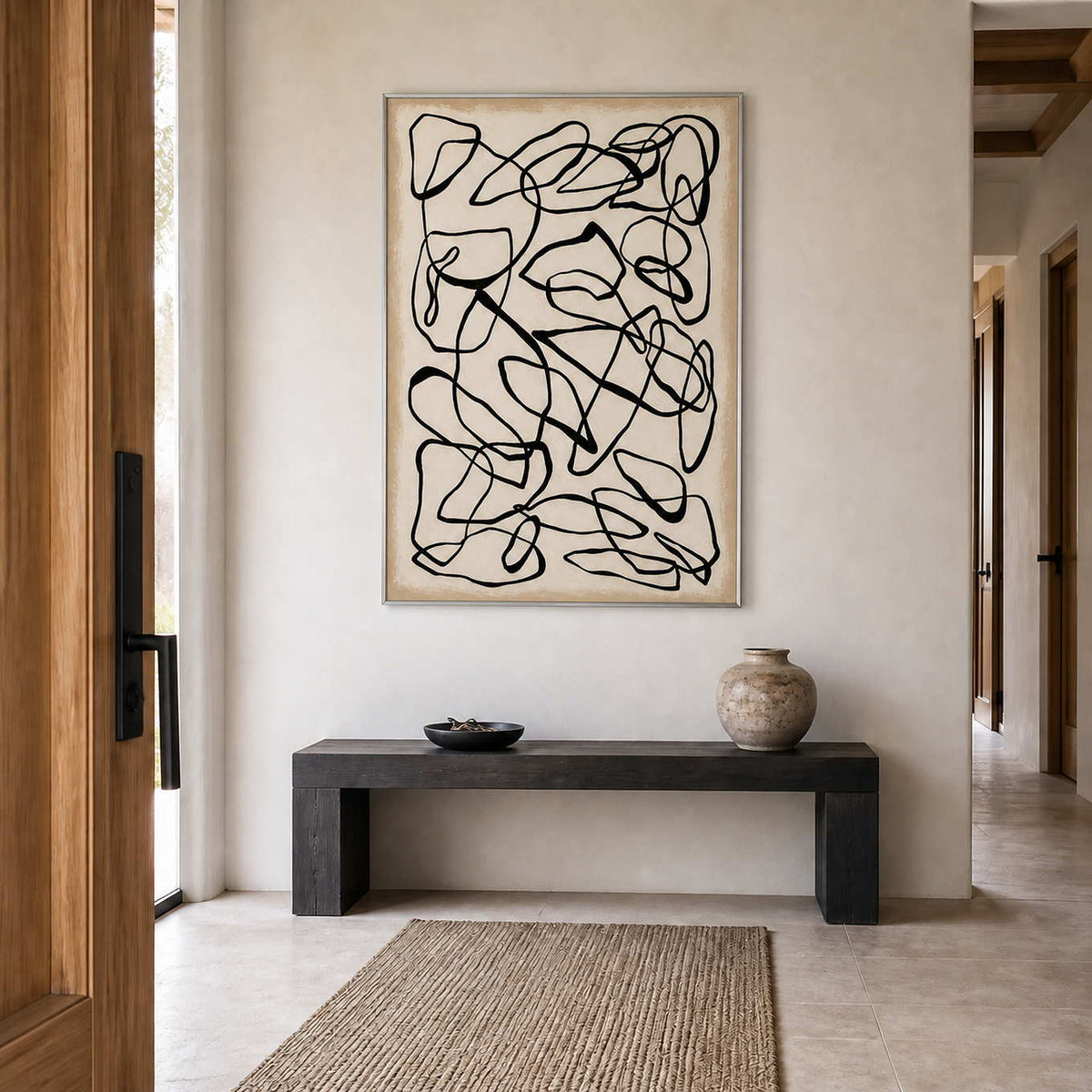 Silver framed black loops above a dark entry console with a ceramic vase.