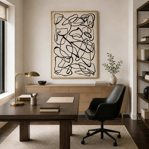 Gold framed line artwork behind a writing desk and black office chair.