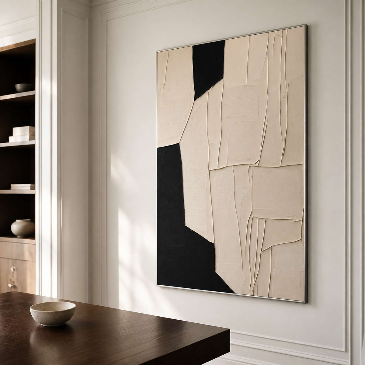 Silver framed cream textured artwork beside a dark wooden desk in a quiet study.