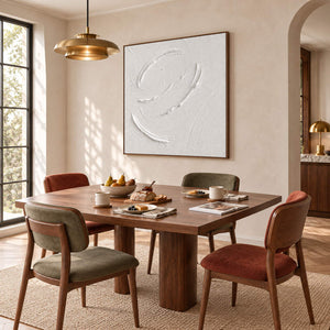 White minimalist relief painting with raised circular gestures in a brown wood frame in a dining room.