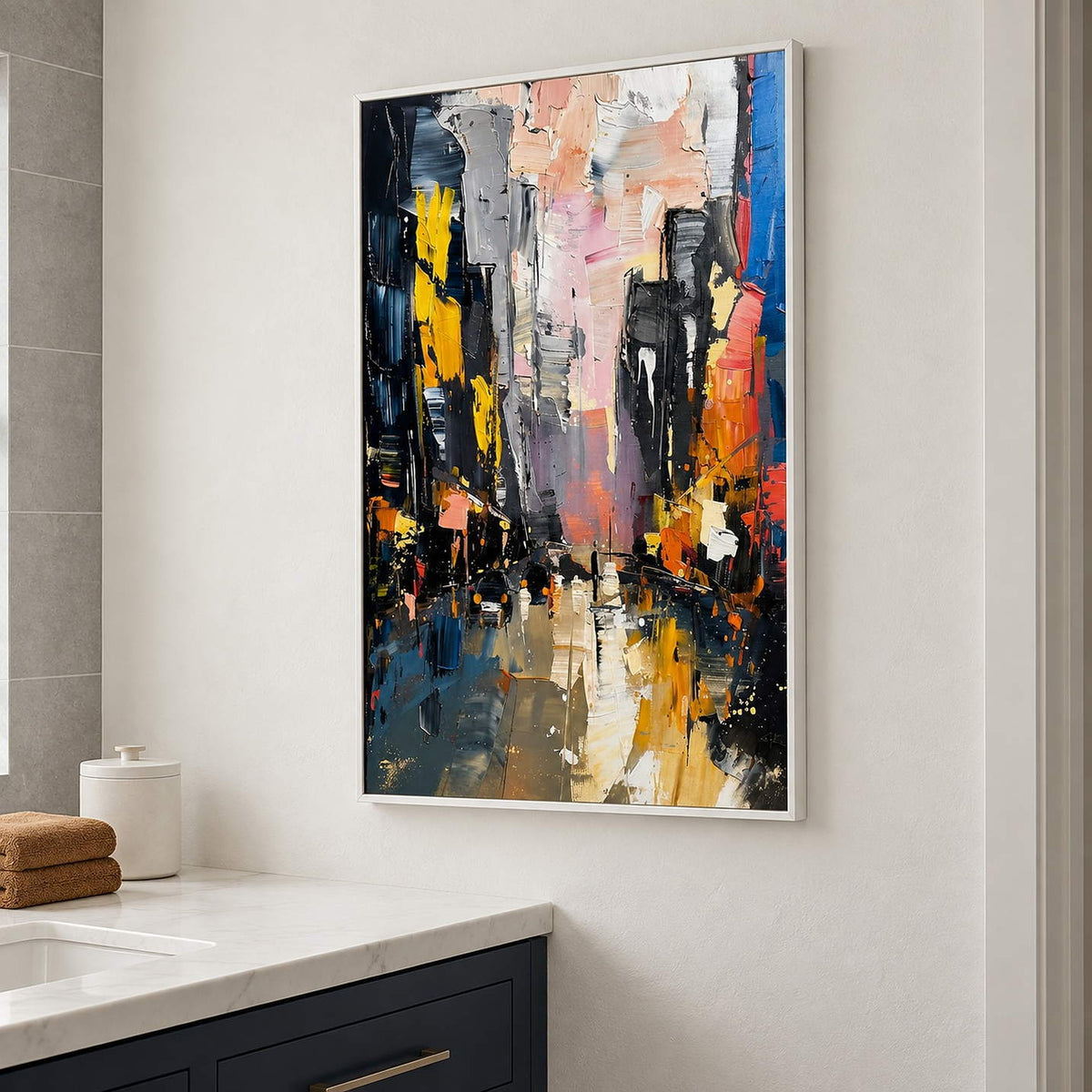 Textured rainy city street painting with yellow lights and dark buildings in a white frame beside a bathroom vanity.