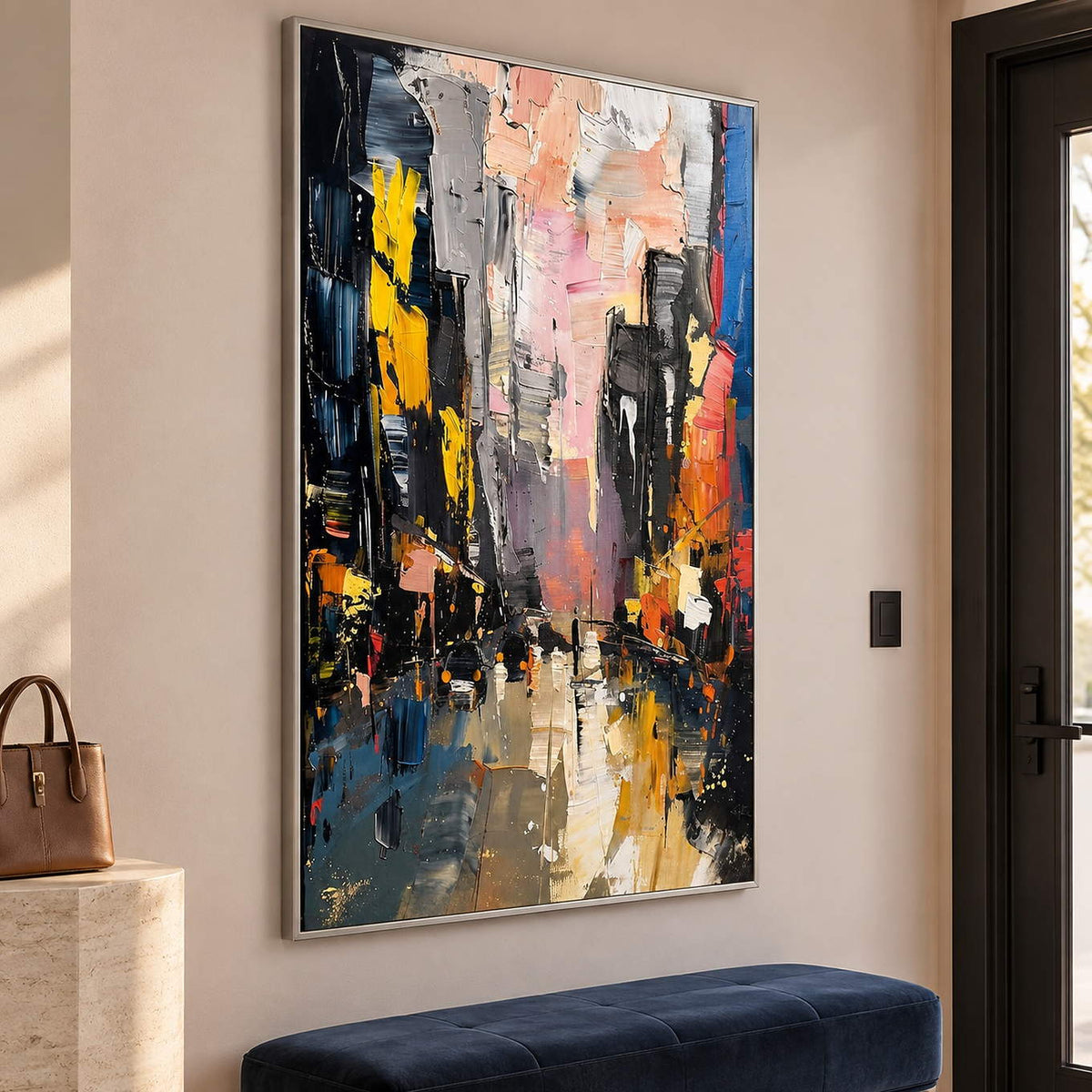Textured rainy city street painting with yellow lights and dark buildings in a silver frame in an entrance hall.