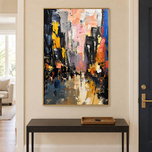 Textured rainy city street painting with yellow lights and dark buildings in a gold frame in an entryway.