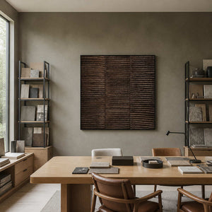 Black framed brown abstract painting beside sample shelves in an architectural studio.