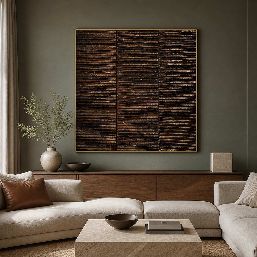 Gold framed brown ridged painting above pale sectional seating in a living room.