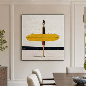 Black framed surfer artwork beside a wooden dining table with cream upholstered chairs.