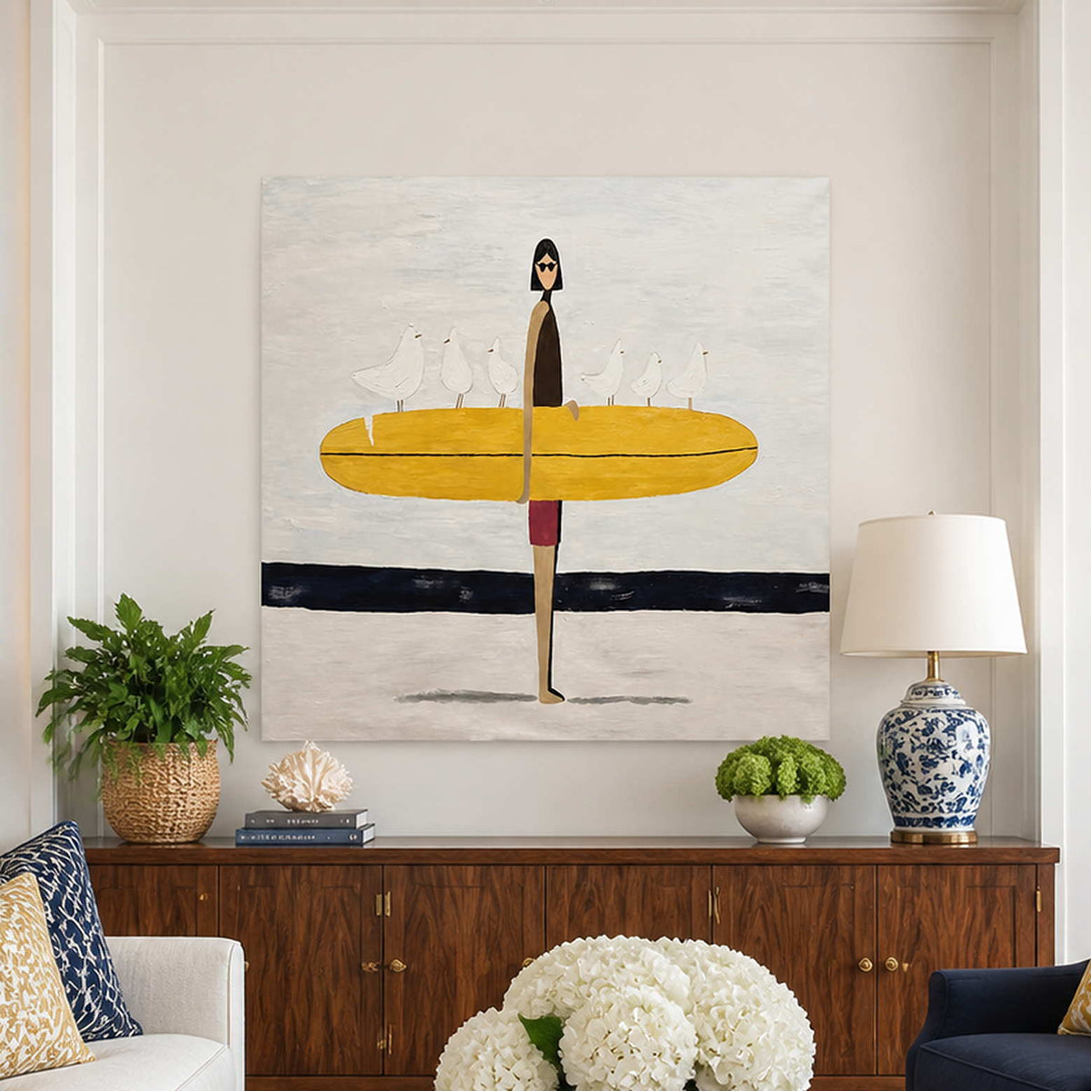 Frameless surfer artwork above a wooden cabinet in a bright coastal living room.