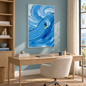 Riding the Wave in a white frame above a light wood desk and cream chair against a blue-green wall.