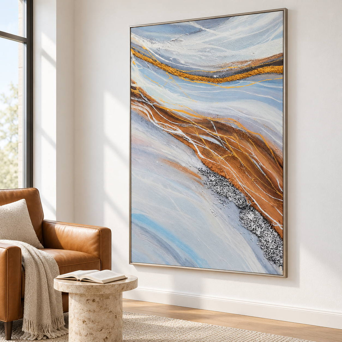 Pale blue-gray bands curving around ochre areas with fine white lines in an artwork with a silver-colored frame, displayed beside a reading chair.