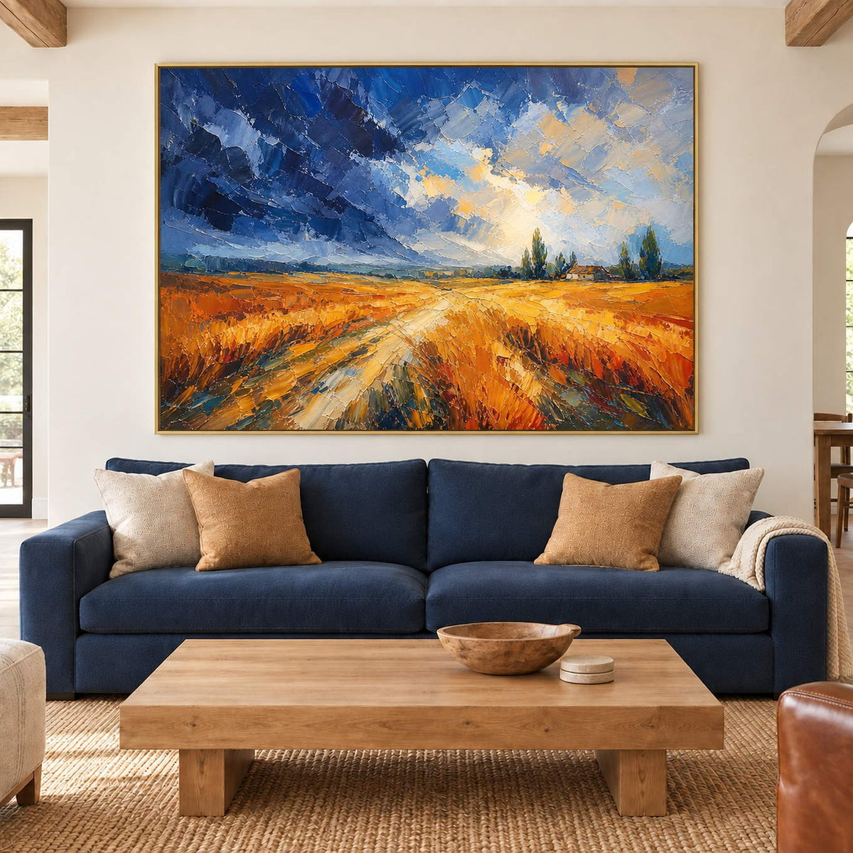 Golden field and winding path painting beneath a blue and cream sky in a gold frame in a living room.