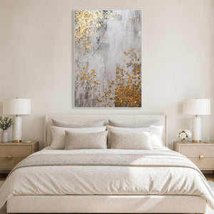 White framed gray and gold abstract artwork above a bed with cream pillows.