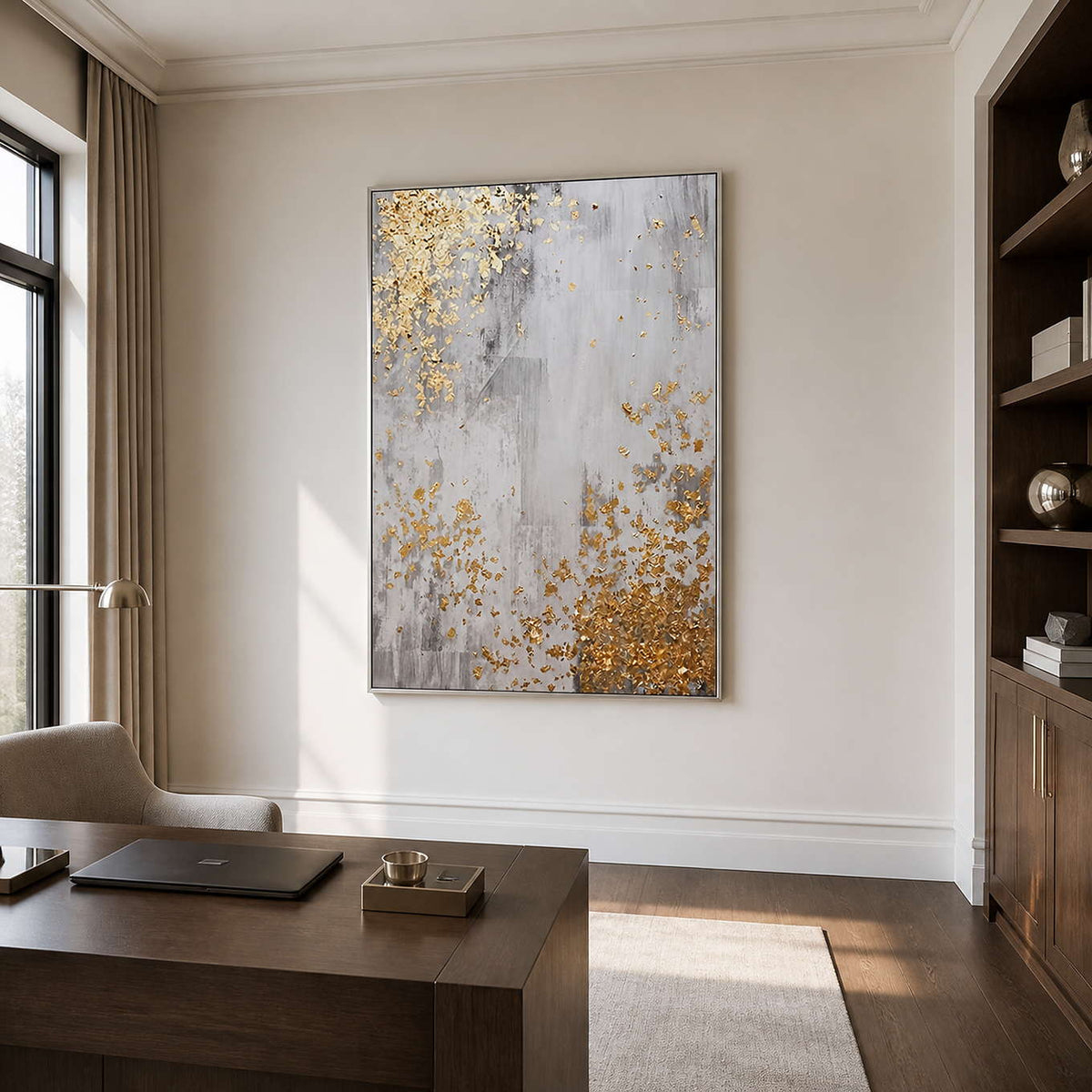 Silver framed gray and gold abstract artwork above a desk beside dark bookshelves.